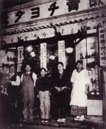 　創業当時の店舗の前で写真に納まる、舟橋義雄に抱かれる政男現名誉会長（左端）ら関係者＝現在の東京都杉並区