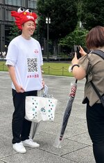 カニのかぶり物とＱＲコードがデザインされたＴシャツを身に着け、撮影に応じる畑先課長