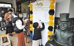 水木さんのブロンズ像の横に設置されたボードに鬼太郎などのイラストを描く観光客＝３０日、境港市本町