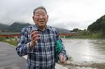 　阿賀野川沿いで当時の様子を語る皆川栄一さん＝２０２５年４月、新潟県阿賀町