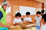 作ろう会のメンバー（左）の指導で伯州綿の茎の液を使った和紙作りを体験する児童