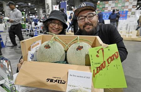　初競りで２玉１００万円で落札された「夕張メロン」。後方は落札した「サンウロコ鱗商会」の柏崎慎太郎取締役（右）ら＝２６日午前、札幌市