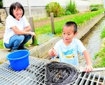 近くの用水路で生き物を捕まえて喜ぶ敬真君（右）を見守る白水さん