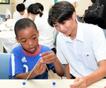 高校生スタッフのアドバイスを受けながらやじろべえ作りに挑戦する児童（左）