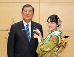　「ミス日本みどりの大使」の佐塚こころさん（右）から緑の羽根を付けてもらう石破首相＝１１日午前、首相官邸