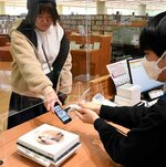 スマホを使って図書を借りる利用者（左）。デジタルサービスの導入により、利便性向上と業務効率化が図られている＝１９日、倉吉市立図書館