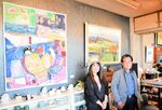 大作「港のノラ」などの作品が飾られた壁の前に立つ佐藤さん（左）と福島さん