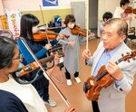 角団長（右手前）の指導でバイオリンを学ぶ参加者