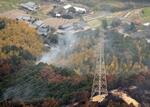 　送電線や住宅地の近くで白煙が上がる山林火災現場＝２７日午後３時４３分、愛媛県今治市（共同通信社ヘリから）