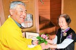 石井会長（左）から花のプレゼントを受け取り顔をほころばせる中村さん＝３月３０日、香美町村岡区長須