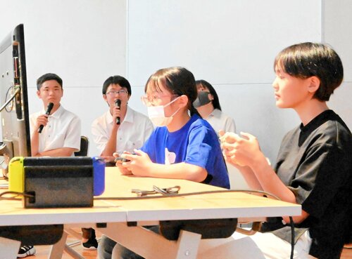 ゲームで対戦する参加者と実況解説する部員（奥）