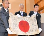 父・行一さんの形見の日章旗を広げる火山司さん（中央）＝２５日、日南町霞の町役場