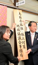 孤独・孤立対策課前に新しい看板を掛ける中島課長（左）ら＝１日、鳥取県庁