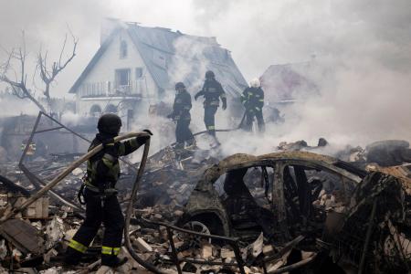 　ロシアの攻撃で破壊された住宅のがれきの中で消火作業を行う作業員ら＝２５日、ウクライナ・キーウ州（ロイター＝共同）