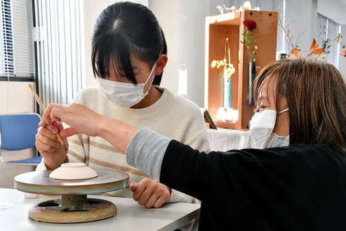 足塚さん（右）から指導を受けながら豆皿に絵付けする参加者＝１９日、鳥取市富安２丁目の日本海新聞ビル５階ホール