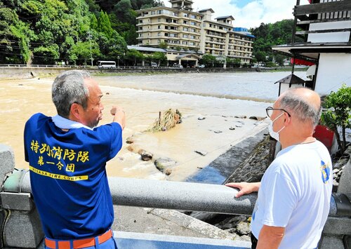 増水した三徳川の濁流に埋没した河原風呂の状況を確認する関係者＝１６日午前１１時半、鳥取県三朝町の三朝温泉街