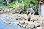 【土砂撤去】裏山が崩落し、車庫前の土砂をかき出す住民＝１６日午後１時１０分、鳥取市佐治町高山