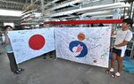 古田選手の活躍を願うメッセージが書かれた国旗と南部町旗を掲げる父親の浩明さん（中央）と母親の尚子さん（左）＝２５日、米子市西町の鳥取県立米子艇庫