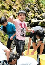岩陰のヤマメをつかみ取り、うれしそうに掲げる参加者