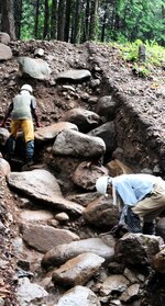 尾高城跡の本丸と二の丸の間にある本丸北堀の石垣を調査する市職員＝２０２２年８月、米子市尾高（市提供）