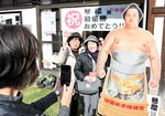 初優勝を祝う横断幕の前で等身大パネルと並んで写真を撮影する相撲ファンら＝２５日、倉吉市魚町の琴桜記念館