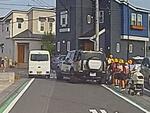 　埼玉県三郷市の市道で、小学生らの脇に止まった車（右）＝１４日午後（住民提供）