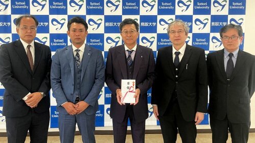 太田社長（左から２人目）から贈られた目録を手にする原田学長（中央）