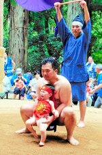 大人の力士に抱えられて土俵入りする稚児