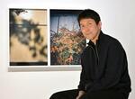 　個展「カスババ　この日常を生きのびるために」で草花を写した作品の前に座る鷹野隆大さん