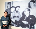 キリノ元大統領（写真手前右）と握手する加納莞蕾の写真の前に立つ佳世子さん。写真は加納美術館で開催中の「人間、加納莞蕾」展で展示されている