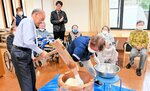 職員らのきねの動きに合わせて手拍子やかけ声で餅つきを楽しむ利用者（奥）＝２６日、香美町香住区森のデイサービスセンターしいの木荘