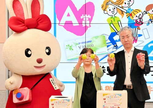 日本海新聞マスコットキャラクターみみちゃんが見守る中、抽選した番号ボールを示す（左から）中松副会長、小谷総局長＝倉吉市上井町１丁目の日本海新聞中部本社