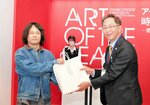 斎藤副館長から記念品を受け取る田中さん（左）＝９日、倉吉市駄経寺町２丁目の県立美術館