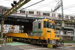 常磐貨物線の踏切を通過するレール運搬車と高架橋を走る京成電鉄の電車