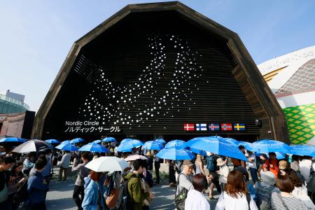 　大阪・関西万博の開幕後初の夏日となり、北欧館が貸し出した日傘を差して並ぶ来場者＝１９日午後、大阪市此花区の夢洲