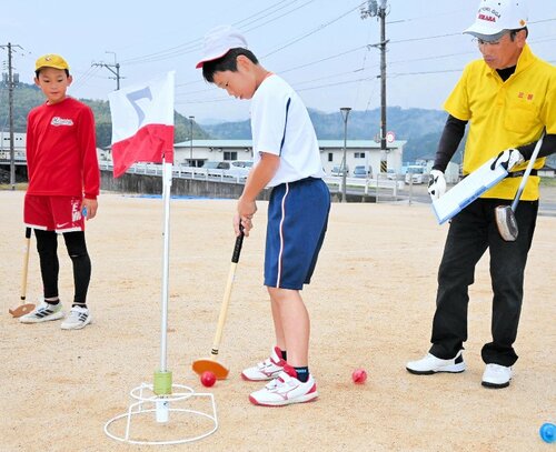 協会員（右）の指導を受けながら新しいクラブを使ってプレーする児童ら
