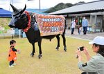 【いい思い出】ハロウィーン仕様に飾り付けられた但馬牛のオブジェの前で記念撮影をする親子。いい思い出になったね