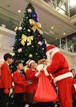 ツリーの前でサンタクロースからプレゼントを受け取る合唱団員＝５日、鳥取市の鳥取砂丘コナン空港