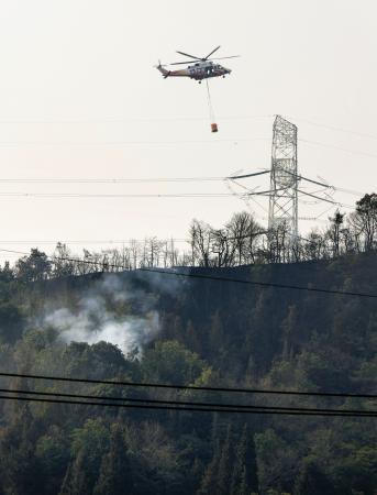 　岡山市南区の山林火災現場で消火活動を行うヘリコプター＝２５日午前９時９分