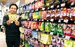 　約１１０種類のグミが並ぶ「ライフ川崎塚越店」の売り場で、独自ブランド商品を持つ社員＝２０２５年３月下旬、川崎市