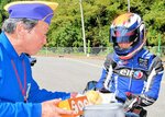 ライダーに梨などを手渡す温泉町ライオンズクラブのメンバー（左）＝２６日、新温泉町千谷の国道９号
