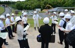 現地視察する審査専門委員ら。建設計画地は奥の駐車場や建物、森林のエリア＝１９日、米子市淀江町小波