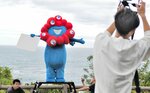  公式ホームページのカウントダウン写真を撮影するミャクミャク（中央）＝２３日、岩美町田後の城原海岸 