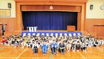 寄贈した式幕の前で児童と記念写真を撮る清水社長（前列右から２人目）ら