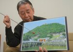 冊子の表紙になった復元写真を説明する神谷さん。実際の風景写真に違和感なく鳥取城を組み合わせている
