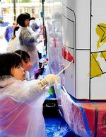 路線バスの車体に筆やはけを走らせる子どもたち＝１９日、ＪＲ鳥取駅前のバード・ハット