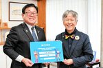 広田市長に巨大パスポートを手渡し、子どもたちの来館を呼びかける稲嶋社長（右）