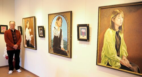 野津さんと、身近な女性や風景などを描いた油絵が並ぶ会場