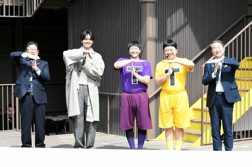 【美術館を盛り上げティー！】　県立美術館ロゴに使われている「Ｔ」を掲げ、パレード開会式を盛り上げるＧＥＮＥＲＡＴＩＯＮＳの片寄涼太さん（左から２人目）と、チョコレートプラネットの長田庄平さん（同３人目）と松尾駿さん（同４人目）ら＝３月２９日、倉吉市明治町の打吹回廊