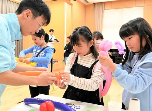 高校生（左）の手を借りながらバルーンアートを楽しむ子どもたち